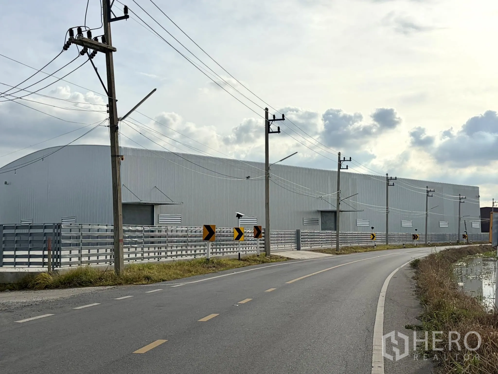 Factory for rent in Uthai, Phra Nakhon Si Ayutthaya - Modern metal-clad factory exterior along a paved road with perimeter fencing and power poles.