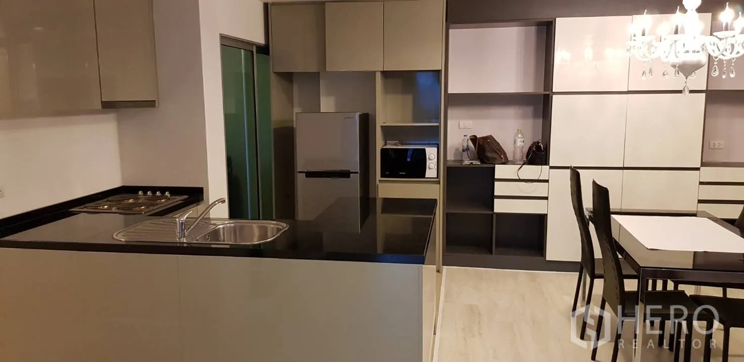 Condominium for rent in Huai Khwang, Bangkok - Open-plan kitchen and dining area with glossy cabinets, refrigerator, microwave and dining set.