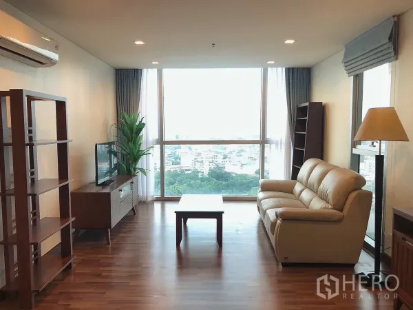 公寓 出租在Khlong Toei, Bangkok - 明亮客厅，落地窗、木地板与皮沙发，享曼谷城市全景。