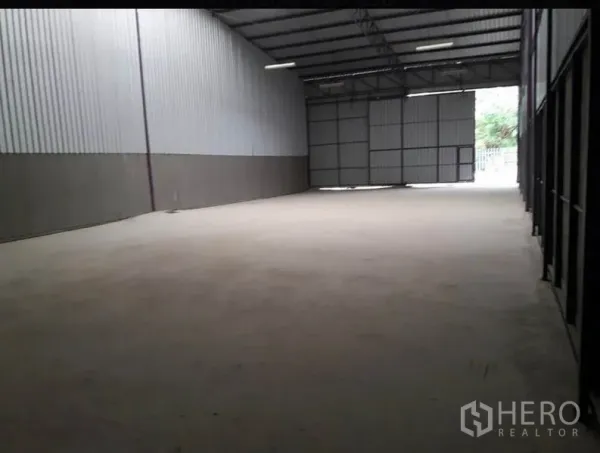 Warehouse for rent in Lam Luk Ka, Pathum Thani - Empty warehouse floor showing metal walls, wide access gate and natural light at the far end.