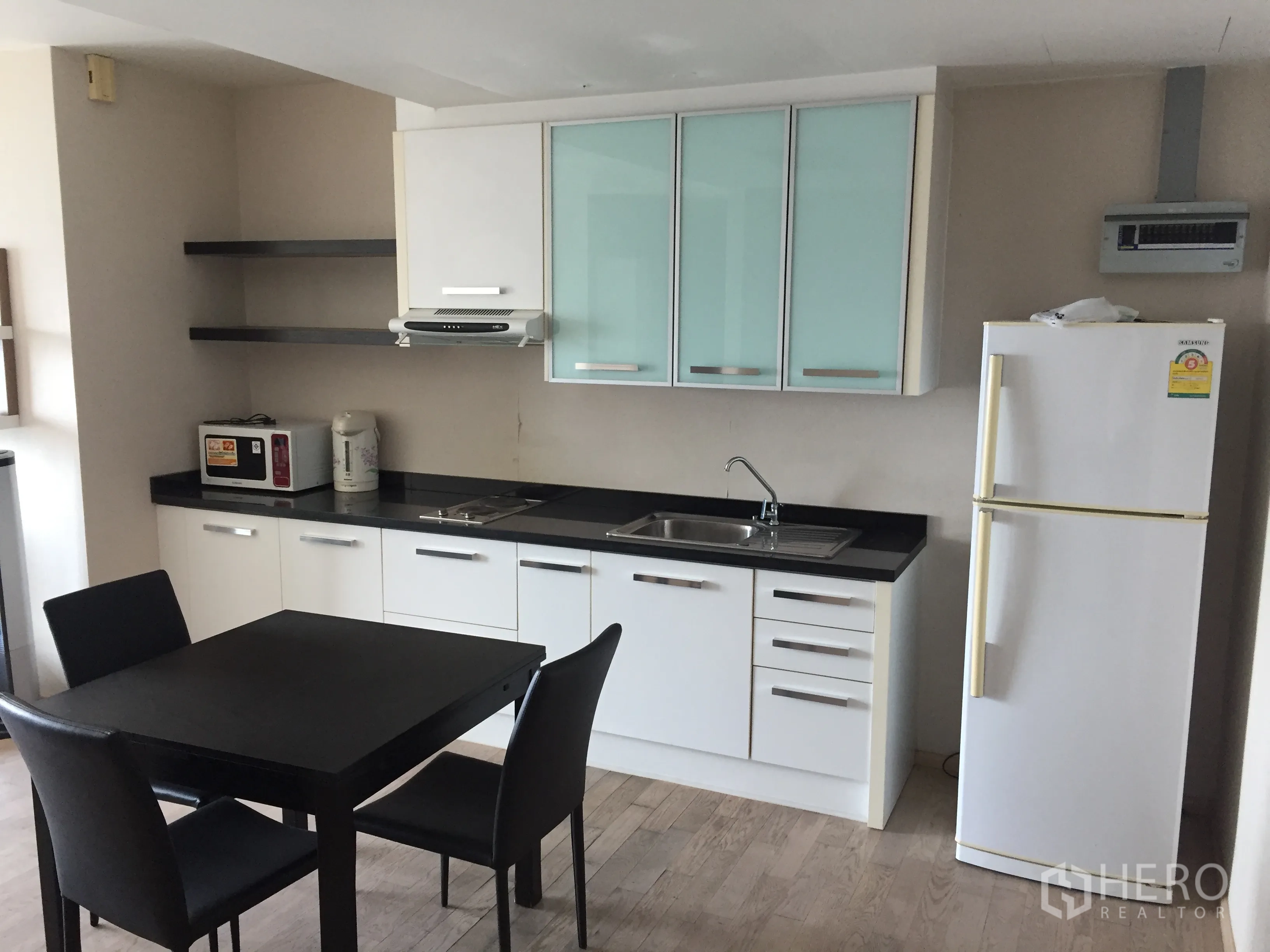 Condominium for rent in Khlong Toei, Bangkok - Modern white kitchen with black countertops, dining table and refrigerator in a Bangkok condo.