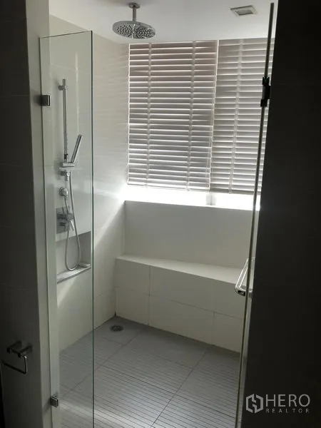 Condominium for rent in Khlong Toei, Bangkok - Bathroom with glass enclosure, rainfall shower and bench by a window with blinds.