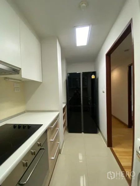 Condominium for rent or sale in Khlong Toei, Bangkok - Kitchen corridor with double-door refrigerator, ample cabinets and bright lighting.