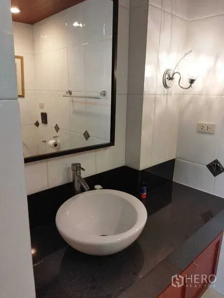 公寓 出租在Pathum Wan, Bangkok - 浴室洗手台，圆形台盆、黑色台面与墙面镜，白色瓷砖。