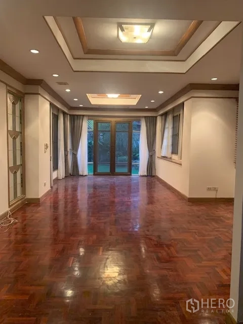 独立式住宅 出租在Khan Na Yao, Bangkok - 细长客厅，拼花木地板、错层吊顶、筒灯，玻璃门通向花园。