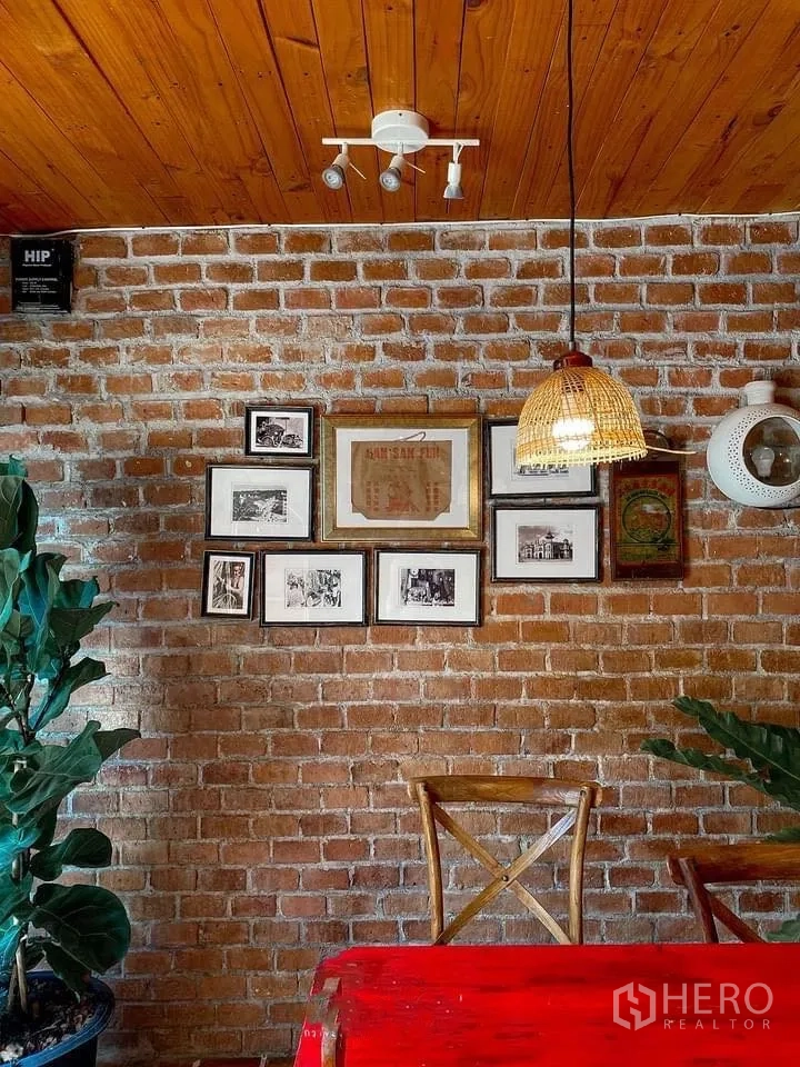 Retail Space for rent in Watthana, Bangkok - Cozy dining corner with exposed brick wall, framed vintage photos, and a rattan pendant over a red table.