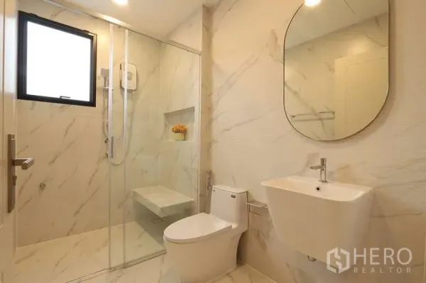 Detached House for rent in Saphan Sung, Bangkok - Modern bathroom with marble-style tiles, glass shower enclosure, toilet and wall-mounted sink.