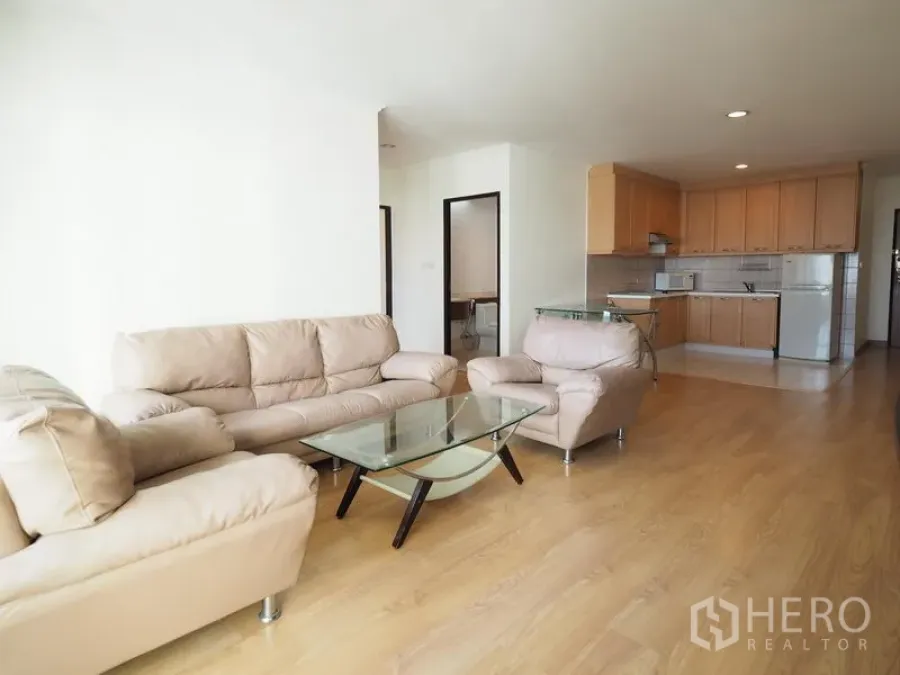 Condominium for rent in Sathon, Bangkok - Spacious living room facing a light-wood kitchen with glass coffee table and neutral sofas in a Sathon condo.