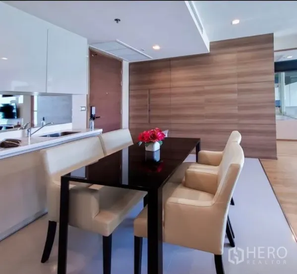 Condominium for rent in Bang Rak, Bangkok - Modern dining area with glossy table, beige chairs and open kitchen.