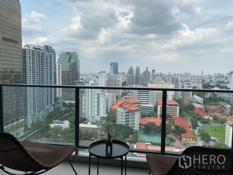 Condominium for rent or sale in Watthana, Bangkok - Covered balcony with two chairs and a small table overlooking the cityscape and greenery.