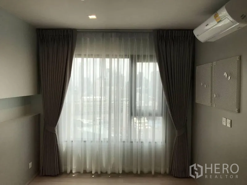 คอนโด ขาย - หน้าต่างห้องนอนพร้อมม่านโปร่งและม่านทึบ มองเห็นวิวเมือง ใต้ไฟดาวน์ไลท์และเครื่องปรับอากาศ