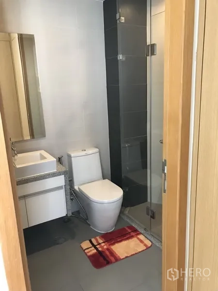 Condominium for rent in Khlong Toei, Bangkok - Contemporary bathroom with glass-enclosed shower, vanity and toilet.