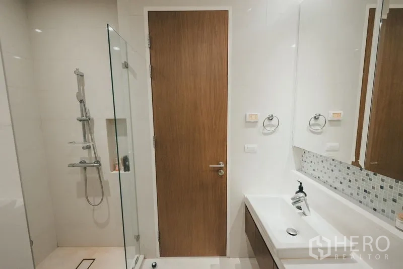 Condominium for rent in Khlong Toei, Bangkok - Modern bathroom with glass-enclosed shower, rain head and extended vanity.