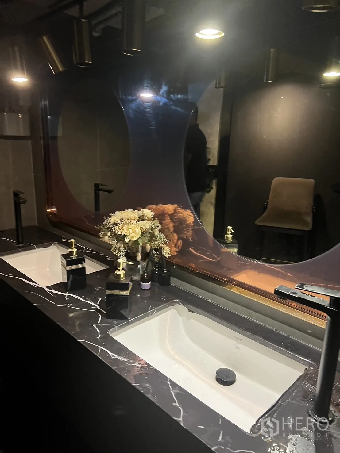 Shophouse for rent in Watthana, Bangkok - Restroom vanity with twin sinks, dark marble countertop and sculptural mirror.