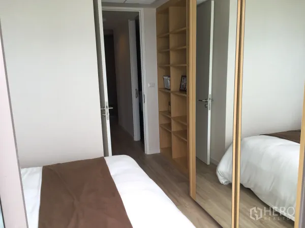 Condominium for sale in Bang Rak, Bangkok - Cozy bedroom with built-in shelves and mirrored wardrobe on light wood flooring.