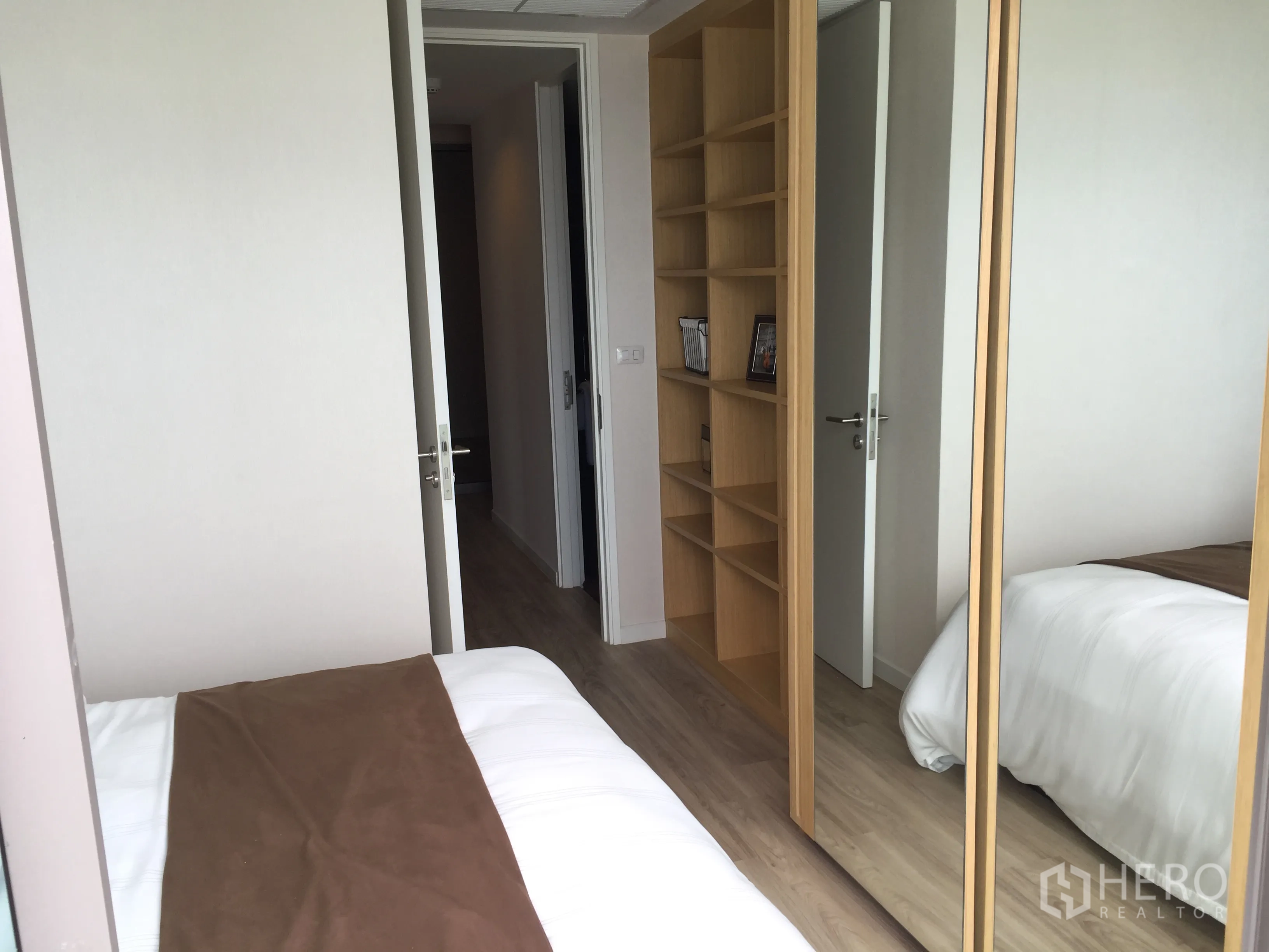 Condominium for sale in Bang Rak, Bangkok - Cozy bedroom with built-in shelves and mirrored wardrobe on light wood flooring.