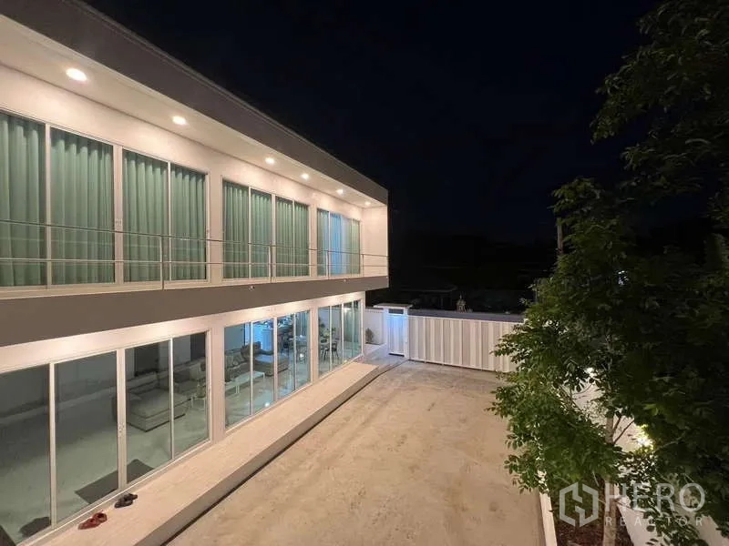 Detached House for rent in Lat Krabang, Bangkok - Courtyard view of the glass‑fronted two‑storey home lit up at night.