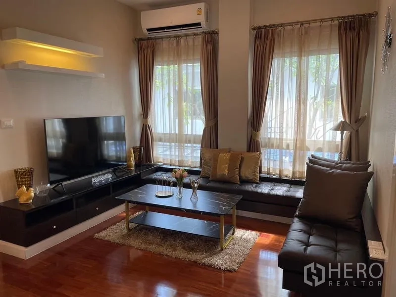 Detached House for sale in Lat Krabang, Bangkok - Living room with TV wall, built-in bench seating and large curtained windows.