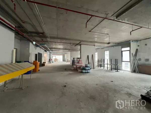 办公空间 出租在Khlong Toei, Bangkok - 狭长型楼层布局，多扇窗户，现场堆放建材与设备。