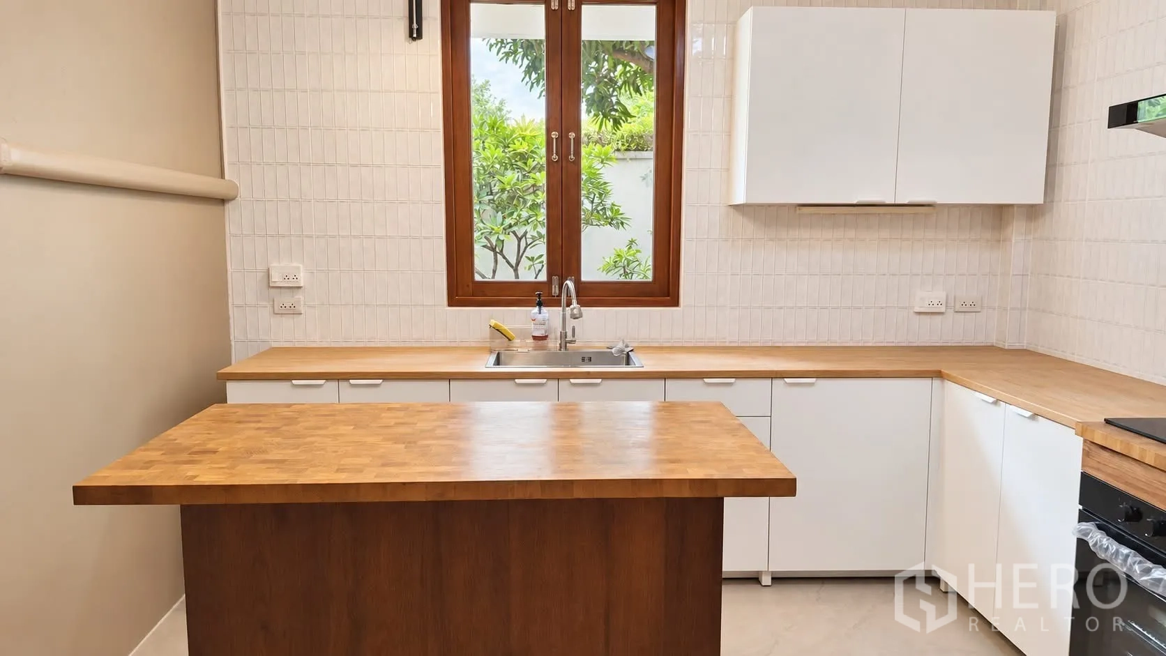 บ้านเดี่ยว for rent in Khlong Toei, Bangkok - ครัวสมัยใหม่พร้อมหน้าต่าง ตู้สีขาว ท็อปไม้ และเกาะกลาง