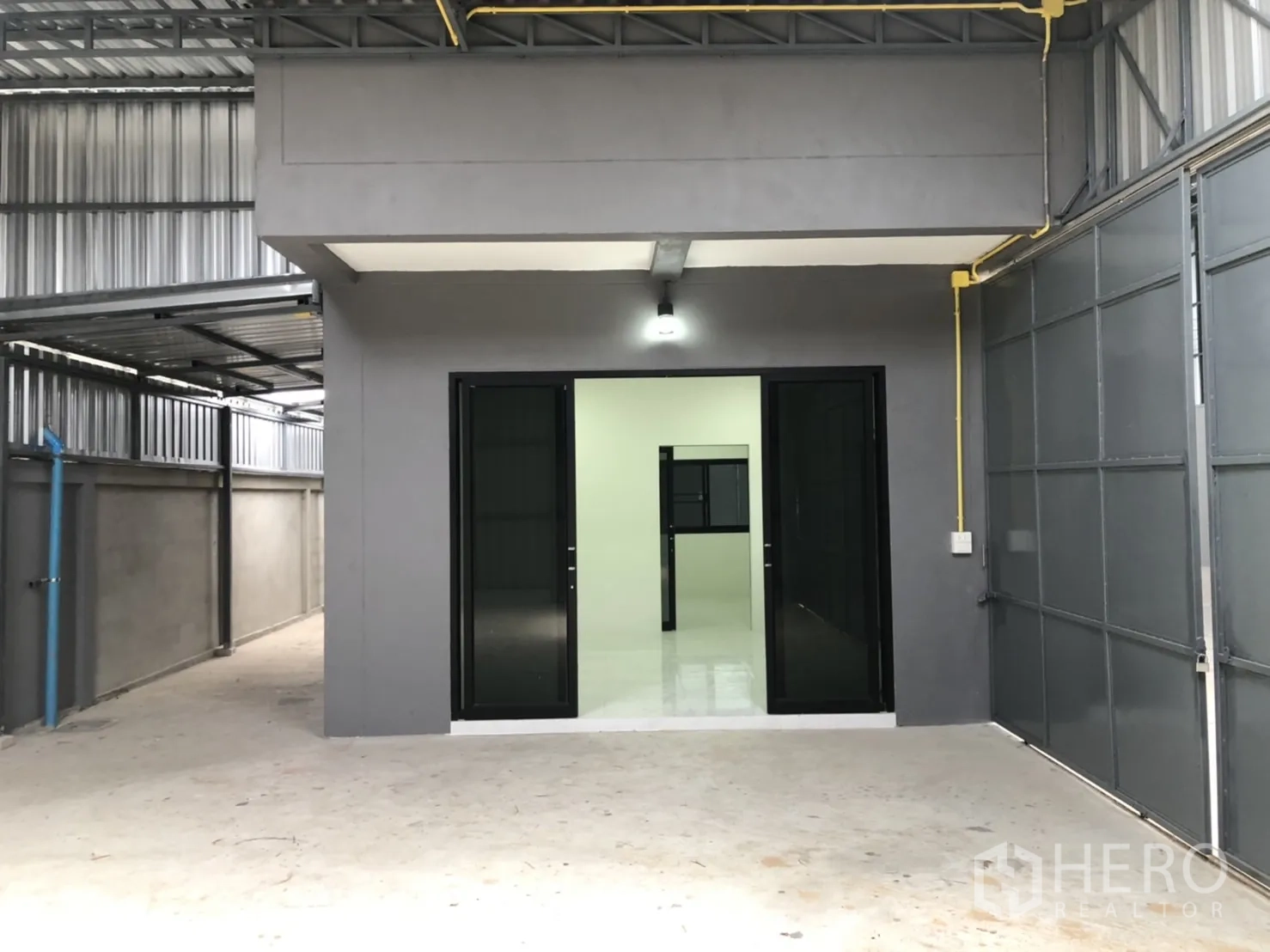 Warehouse for rent in Lam Luk Ka, Pathum Thani - Office facade within the warehouse, black-framed glass doors beside a large metal gate.