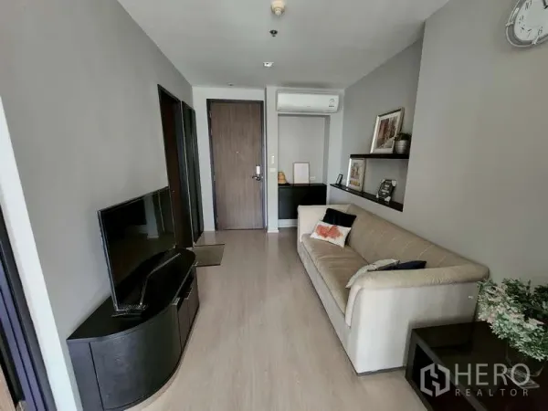 Condominium for sale - Bright living room with TV console, beige sofa, wood flooring, shelves and air conditioning by the entry door.