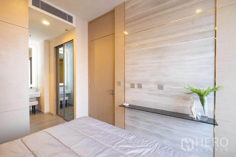 公寓 出租在Watthana, Bangkok - 卧室墙面饰板与窄置物台，镜面衣柜及通往梳妆区和卫生间的门。
