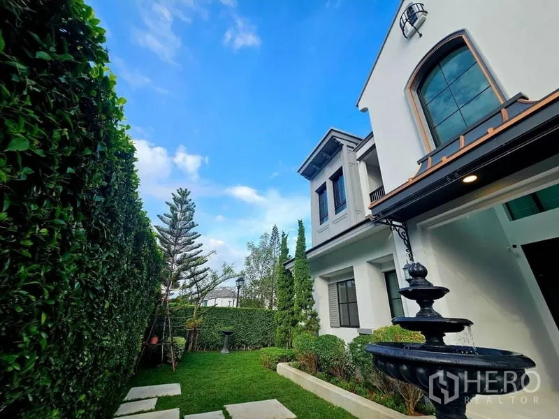 Detached House for rent or sale in Saphan Sung, Bangkok - Private side garden with fountain, clipped hedges and a stepping‑stone path beside the house.