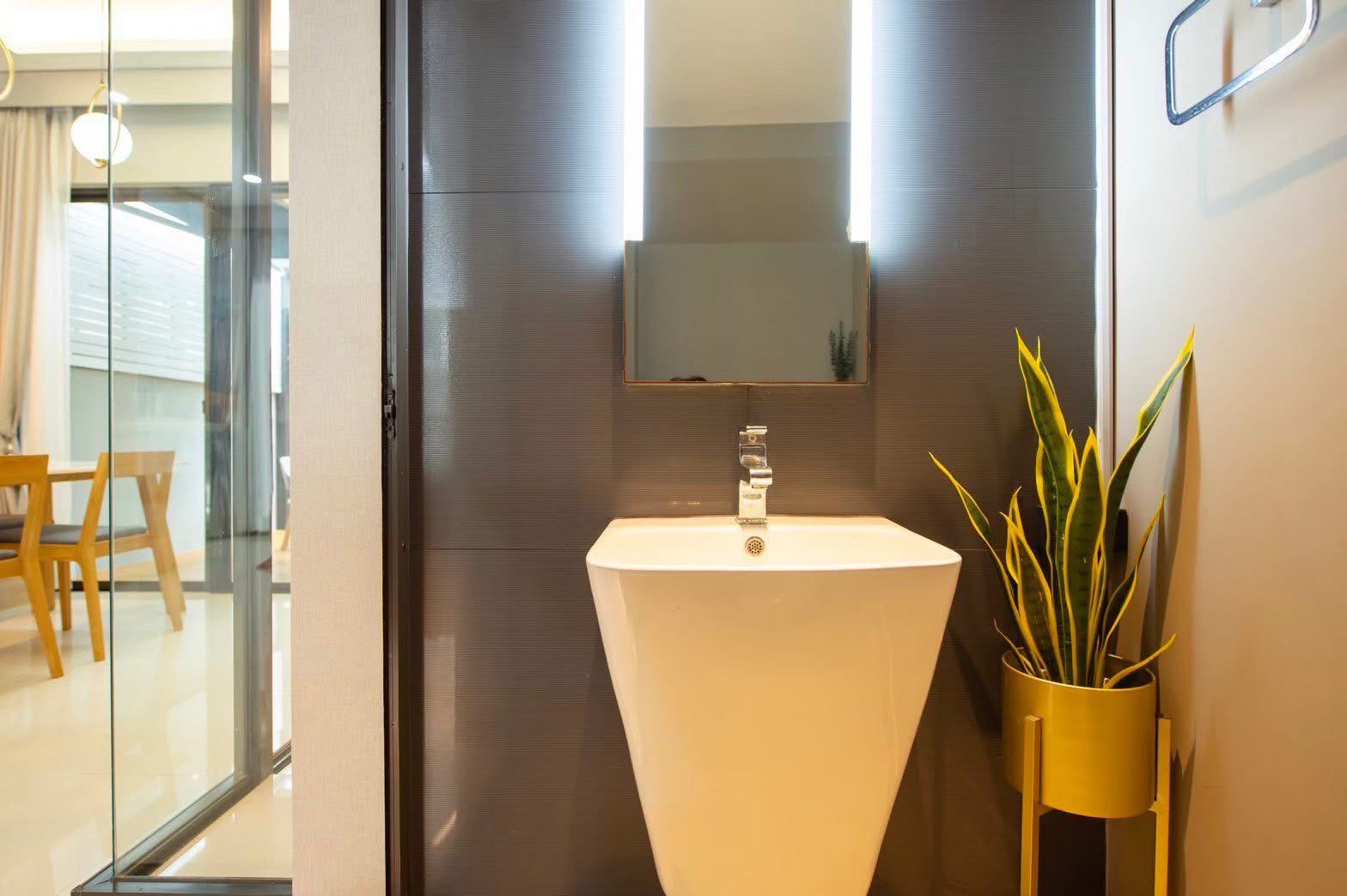 Townhouse for rent or sale in Lat Phrao, Bangkok - Bathroom vanity with tall backlit mirror and modern pedestal sink with a plant in a yellow stand.