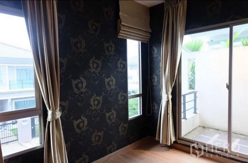 บ้าน ให้เช่าในSuan Luang, Bangkok - ห้องมุมผนังลายวอลเปเปอร์สีเข้ม มีหน้าต่างสูง และประตูกระจกเปิดสู่ระเบียงเล็ก