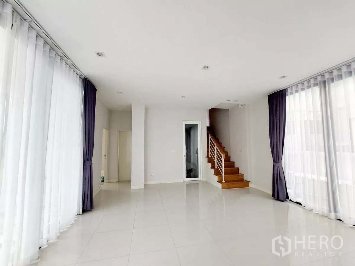 Townhouse for rent in Lat Phrao, Bangkok - Sunny ground-floor lounge with multiple sliding glass doors and a stairway to the upper floors.