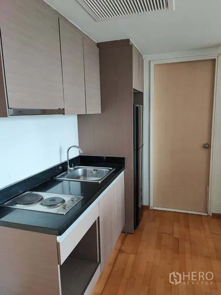 Condominium for sale in Khlong Toei, Bangkok - Compact kitchenette with electric hob, double sink, upper cabinets and refrigerator.