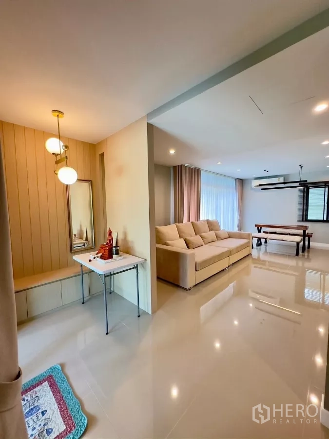 Detached House for rent in Samut Prakan - Open-plan living with large beige sofa, glossy floor and floor-to-ceiling curtains.