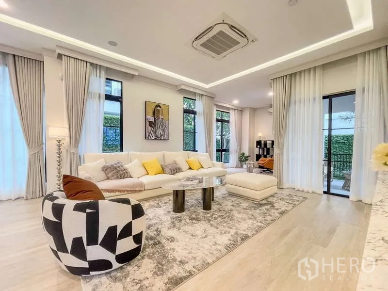 Detached House for rent in Saphan Sung, Bangkok - Airy living room with sectional sofa, tall windows and garden views.