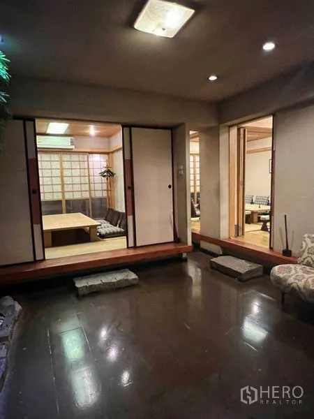 Shophouse for rent in Khlong Toei, Bangkok - Framed view through blossoms into a tatami room with cushions and low table.