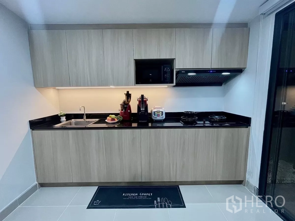 Townhouse for rent in Samut Prakan - Sleek built-in kitchen with wood cabinets, black countertop and under-cabinet lighting.