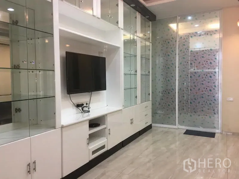 联排别墅 出租在Bang Rak, Bangkok - 白色内置电视柜与玻璃展示架，墙挂电视，磨砂推拉门。