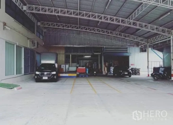 Warehouse for rent in Bang Kho Laem, Bangkok - Covered warehouse loading area with high metal roof, roller shutter door, marked parking bays, and drive-in truck access.