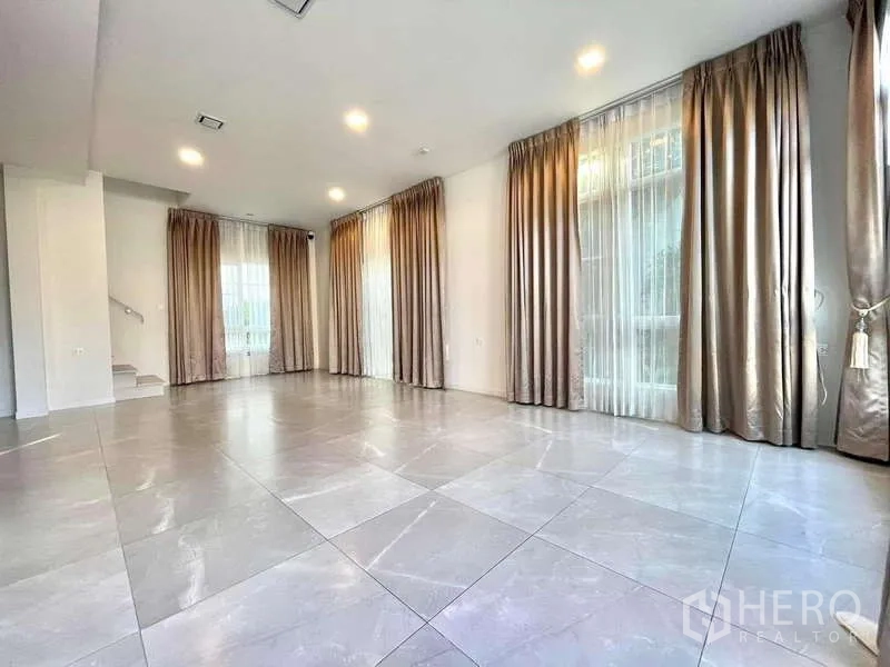 Detached House for rent in Prawet, Bangkok - Spacious living room with large-format tiles, floor-to-ceiling windows, drapes and recessed lighting.