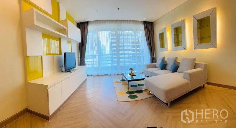 Condominium for rent in Bang Rak, Bangkok - Bright living room with L-shaped sofa, TV console, chevron wood floors, and floor-to-ceiling windows opening to a city-view balcony.