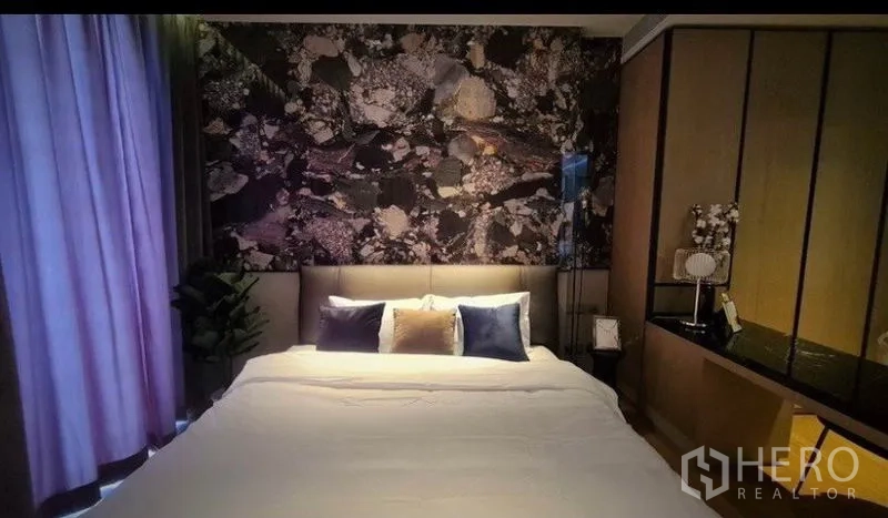 Condominium for rent in Khlong Toei, Bangkok - Bedroom at dusk highlighting the textured feature wall, soft lighting and neatly made bed.