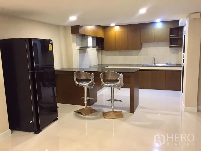 联排别墅 出租在Khlong Toei, Bangkok - 现代厨房，设岛台吧椅、黑色冰箱与嵌入式柜体。