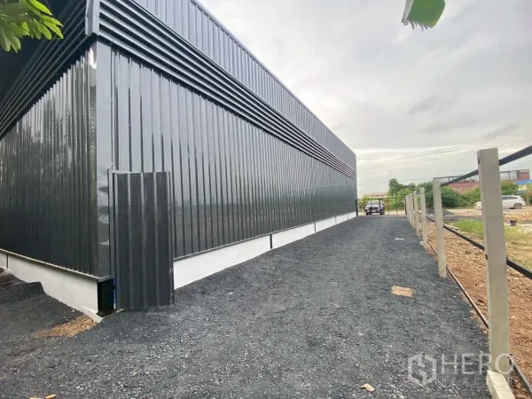 Warehouse for rent in Lam Luk Ka, Pathum Thani - Side access lane beside the metal-clad building leading to a rear gate.