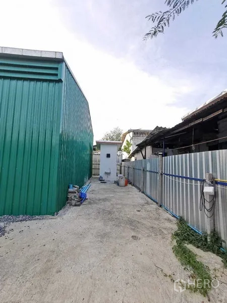 Warehouse for rent in Bang Na, Bangkok - Side yard along green warehouse wall with a small white utility room