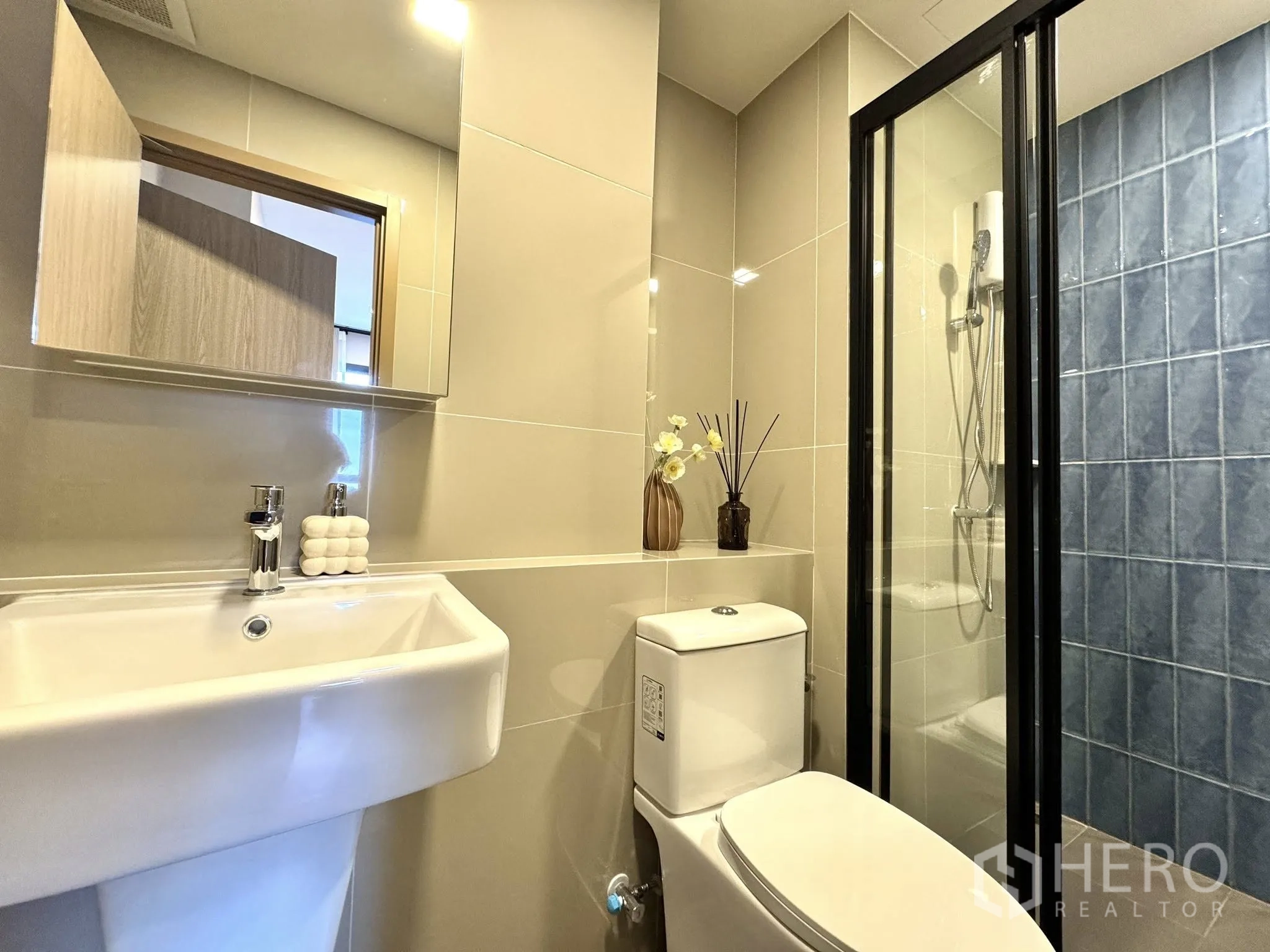 Condominium for rent in Watthana, Bangkok - Modern bathroom with glass shower enclosure, blue tile accent wall, and vanity.