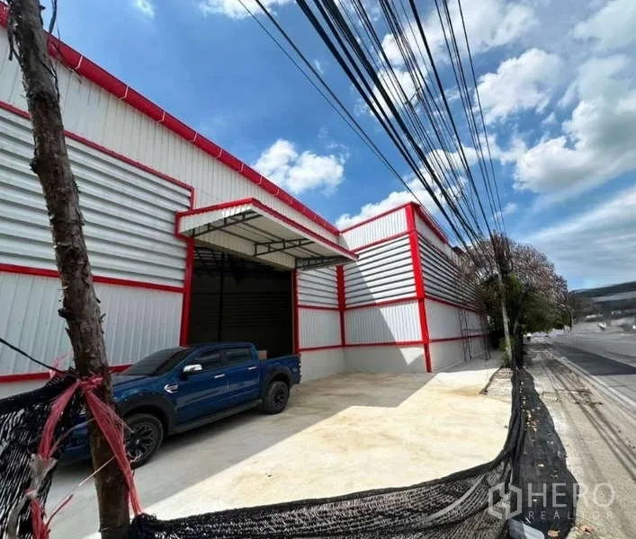 Warehouse for rent in Sai Mai, Bangkok - Street-side view of a modern red-trim warehouse with a large roller shutter and covered loading bay.