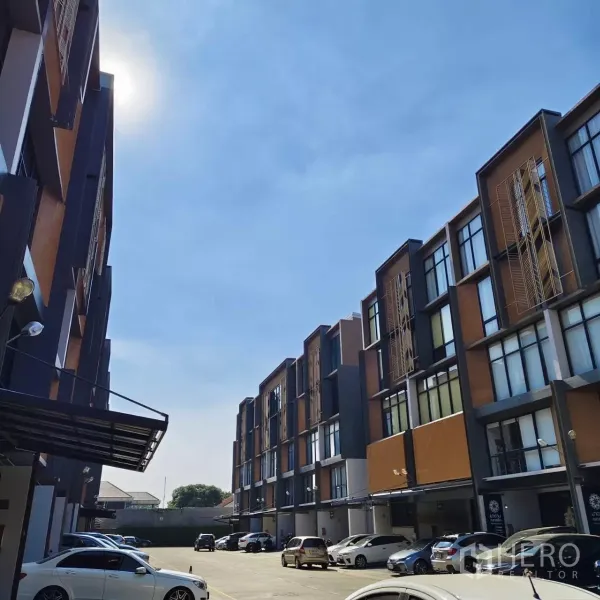 带办公室的家 出租或出售在Watthana, Bangkok - 成排低层家办建筑与地面停车区，晴朗天空下的园区景观。
