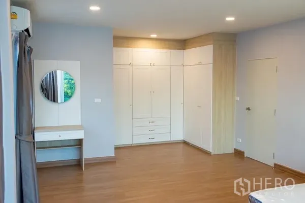 Detached House for rent in Bang Phli, Samut Prakan - Spacious bedroom with built-in white wardrobes, vanity and wood flooring.