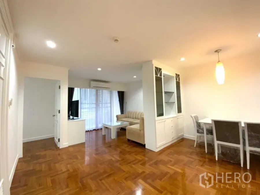 公寓 出租在Watthana, Bangkok - 客餐厅一体空间，拼花木地板，米色沙发组、电视柜与通往阳台的玻璃门。