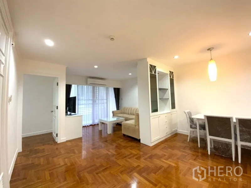 公寓 出租在Watthana, Bangkok - 客餐厅一体空间，拼花木地板，米色沙发组、电视柜与通往阳台的玻璃门。